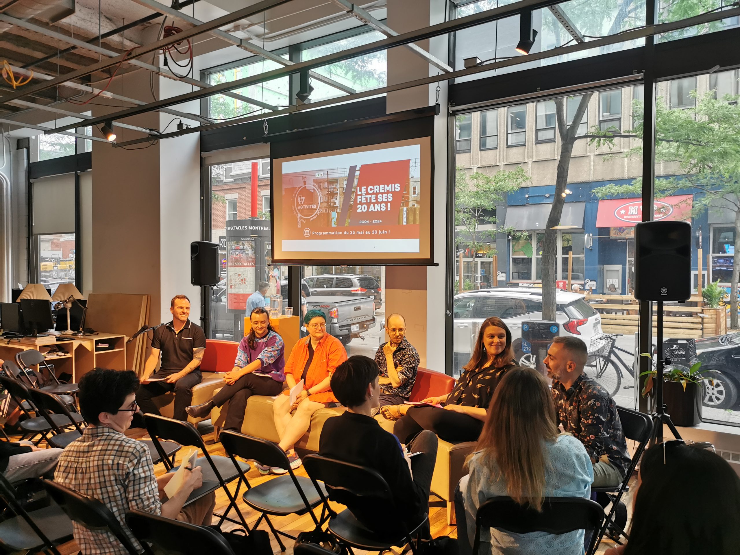 À l'espace ville autrement, lors de l'événement « Décloisonner les savoirs : la recherche communautaire LGBTQ ». Vue sur les panélistes et sur la rue Sainte-Catherine en arrière, à travers une baie vitrée.